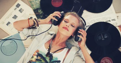 A young woman listening to music while lying on her back and surrounded by records